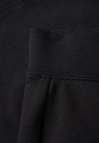 Schwarzer Baumwollstoff mit glatter Textur, der eine Naht und ein umgeschlagenes Bündchen zeigt. Das Design ist minimalistisch und einheitlich.