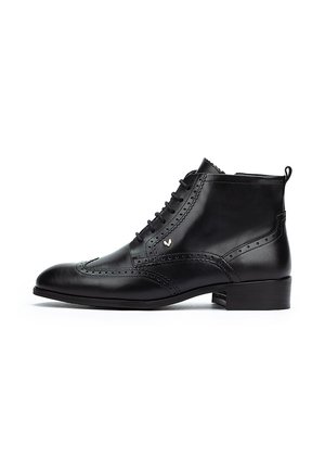 Bottine en cuir noir avec un bout pointu, des détails de brogue décoratifs, un système de laçage à l'avant et un petit talon. Texture lisse avec une accent en or.