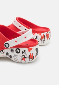Sabots rouges avec des brides blanches, dotés d'une semelle intérieure texturée et d'une semelle à motif représentant Mickey et Minnie Mouse en accents noir et rouge.