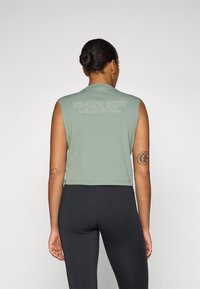 Green sleeveless cropped tank top with "HEALTH BODY MIND SOUL" text, smooth texture, and round neckline, paired with black leggings.