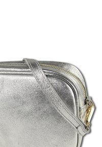 Silberne Metallic-Umhängetasche mit glatter Textur, ausgestattet mit einem goldenen Reißverschluss und Riemen, rechteckiger Form und minimalistischem Design.