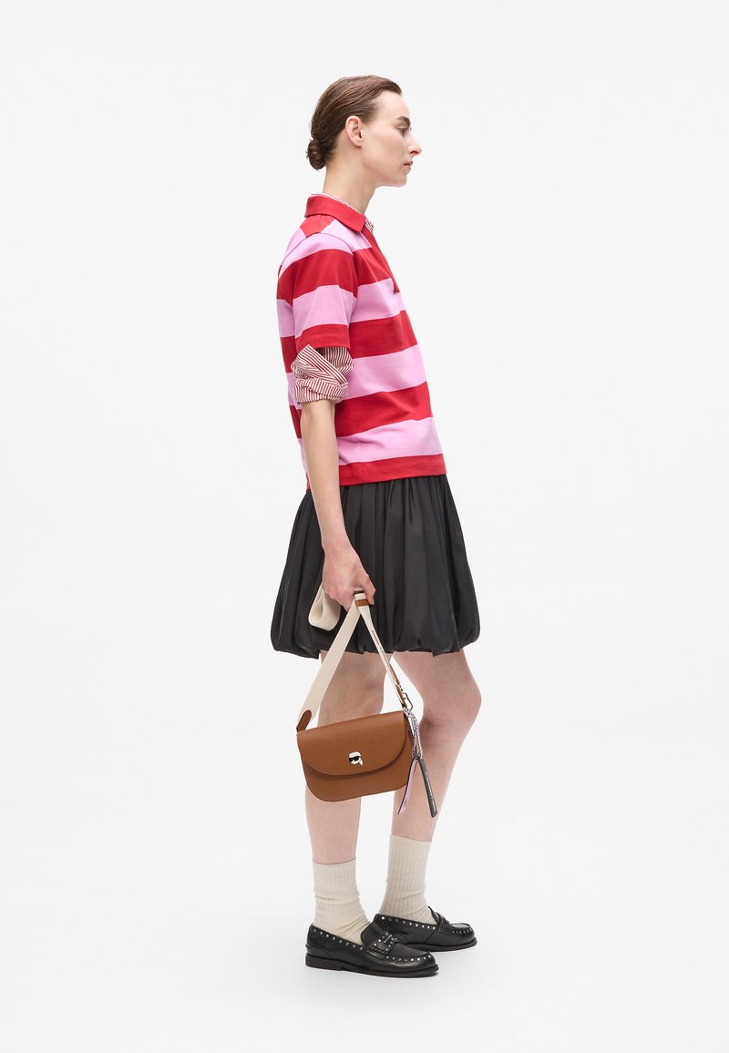 Polo a righe rosse e rosa, gonna plissettata nera, borsa in pelle marrone, calze color crema e mocassini neri con borchie.