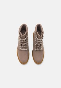 Brown suede ankle boots with round toe, grey laces, silver hardware, and a gum rubber sole. Smooth texture with padded collar.