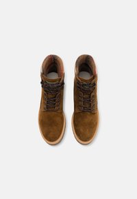 Brown suede ankle boots with dark laces, light brown rubber soles, and patterned lining visible at the top opening.