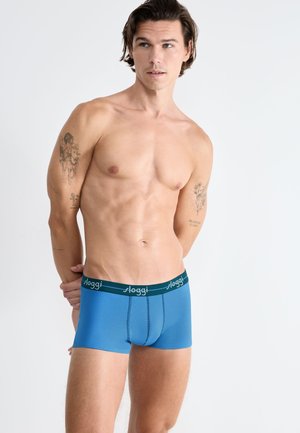 Sous-vêtement bleu de style slip avec une ceinture élastique verte portant un texte de logo blanc. Tissu lisse avec des détails de couture minimaux.