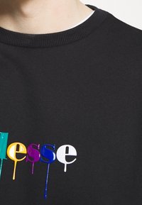 Felpa nera con collo a coste e design di testo gocciolante multicolore in verde, giallo, viola, blu e bianco sul petto.