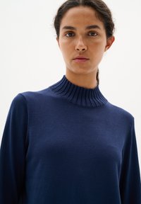 Mörkblå tröja med ribbad hög krage och långa ärmar. Tillverkad av ett mjukt material med en slät yta och en åtsittande design.
