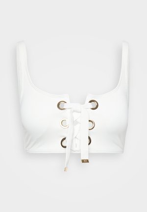 Top en blanc avec de larges bretelles, présentant un devant lacé avec des œillets dorés et un tissu blanc noué. Texture lisse, design simple.