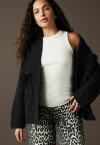Cardigan negru tricotat cu modele texturate peste un top de bumbac cu dungi gri deschis, asortat cu pantaloni bej cu imprimeu leopard.