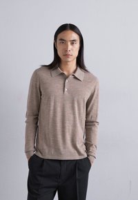 Polo shirt lungo a maniche in un morbido tessuto testurizzato di colore marrone chiaro, con colletto e chiusura a tre bottoni, abbinato a pantaloni scuri.