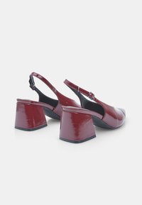 Punase läikega nahast slingback-kÄ±ngad ruudukujulise varbaga ja massiivse geomeetrilise kanna disainiga. Omab reguleeritavat pahkluu rihma.