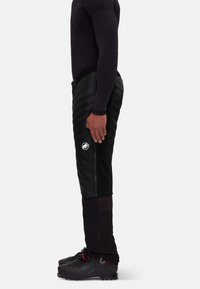 Zwarte geïsoleerde broek met een quilted textuur, zijritsen en een logo-patch, gecombineerd met zwarte schoenen en een aansluitend top.