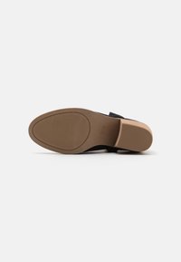 Suela de zapato negra con un patrón texturizado y una plantilla suave. Punta redondeada y un tacón robusto de color marrón claro.