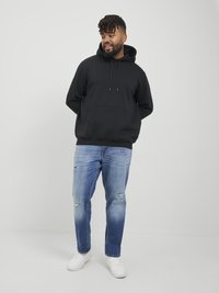 Black hooded sweatshirt with front pocket, paired with light blue distressed jeans and white sneakers. Neutral background, relaxed fit.