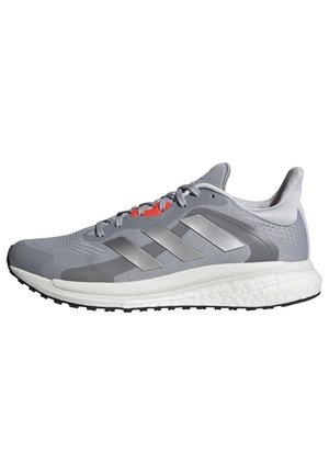 Jasnoszary i biały but do biegania z ciemniejszymi szarymi paskami Adidas, siateczkową cholewką, amortyzowaną podeszwą i czarnym bieżnikiem na spodzie.