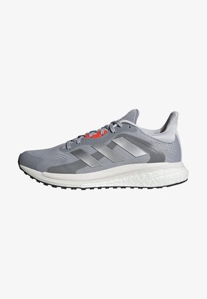 Jasnoszary i biały but do biegania z ciemniejszymi szarymi paskami Adidas, siateczkową cholewką, amortyzowaną podeszwą i czarnym bieżnikiem na spodzie.