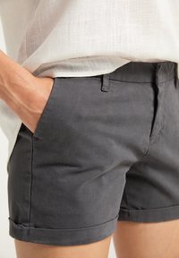 Tummanharmaat puuvillashortsit, joissa on sileä pinta ja käärityt lahkeet, sivutaskut sekä istuva malli.
