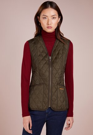 Gilet imbottito di colore verde oliva con zip, dotato di due tasche frontali e rifiniture marroni, indossato sopra un dolcevita rosso e jeans blu.