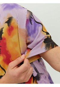 Camisa de manga corta con un vibrante patrón degradado en púrpura, naranja y rojo, con acentos en negro y una tela texturizada y transpirable.