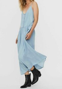 Vaaleansininen hihaton mekko, jossa on nappikiinnitys edessä, väljät helmat ja rispaantunut alaosa, yhdistettynä mustiin teksturoidumpiin nilkkasaappaisiin.