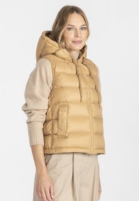 Kamizelka puchowa w kolorze beżowym z kapturem, zamek z przodu oraz dwie boczne kieszenie. Wykonana z materiału w wzory, pikowanego dla izolacji i ciepła.