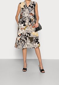 Vestido sin mangas floral con cuello, que presenta una mezcla de patrones en negro, blanco, naranja y amarillo. Incluye bolsillos laterales.
