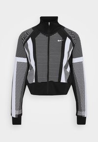 Chaqueta recortada en blanco y negro con un cuello alto, que presenta patrones a rayas y de malla, y un cierre frontal. Logo de Nike en el pecho.