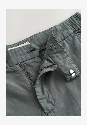 Pelēki bikses ar rāvējslēdzēju, kas izgatavots no misiņa, zilu pogu aizdari un šuvīgu jostasvietu. Mīksta tekstūra ar minimālistisku dizainu.