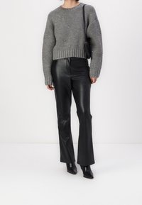 Donna che indossa un maglione di maglia grigia con dettagli in perle, pantaloni di pelle neri, stivali neri con punta affilata e una borsa a spalla nera.