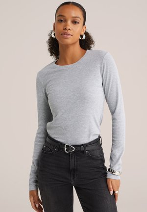 Lichtgrijze langarmshirt met een ronde hals, gecombineerd met zwarte jeans en een zwarte riem met een zilveren gesp. Glad textiel.
