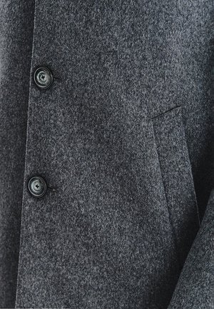 Szary wełniany płaszcz o teksturowanym wykończeniu, z dwoma czarnymi guzikami i jednym ukrytym kieszeniem na boku. Prosty, dopasowany krój.