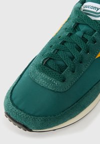 Sneaker verde, care prezintă o combinație de material textil neted și suede texturat. Are un design cu șireturi, accente galbene și o talpă din cauciuc.