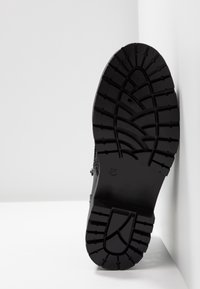 Suela de goma negra con un diseño de tacos profundo, mostrando el tamaño marcado 37. El borde del zapato es redondeado, con una superficie texturizada para ofrecer agarre.