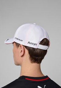 Biała czapka bejsbolowa z czerwonymi akcentami, z logo: TAG Heuer, Ansys i Porsche. Gładki materiał, zakrzywiony daszek i regulowany pasek.
