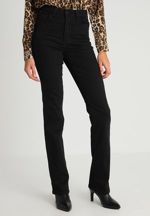 Osoba ubrana w czarne jeansy z wysokim stanem i prostymi nogawkami, czarne botki na obcasie z zaostrzonym noskiem oraz długi top w panterkę z długim rękawem.