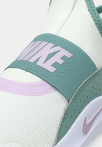 Nike cipele za klizanje s bijelim teksturiranim gornjim dijelom, tirkiznim elastičnim remenom s istaknutim svijetlopurpurnim logotipom i udobnom svijetlopurpurnom potplatom.