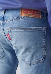 Ljusblå denimjeans med en bakficka och röd Levi's-tag, som visar en brun lädermärke på midjebandet.