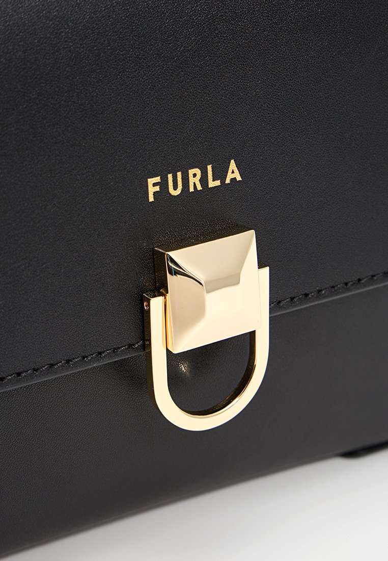 Sac à main en cuir noir avec un fermoir et logo en métal doré. Texture lisse et forme rectangulaire élégante.