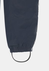 Námořnické modré nepromokavé kalhoty mají elastický pas s šňůrkou a reflexní prvky na bocích pro zvýšení viditelnosti.