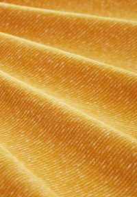 Primer plano de una tela texturizada en un vibrante amarillo con sutiles motas blancas y ondulaciones diagonales, que muestra un diseño suave y tejido.