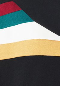 Maglione a maglia con blocchi di colore orizzontali in rosso, verde acqua, bianco e giallo senape su uno sfondo nero; texture morbida, design casual.