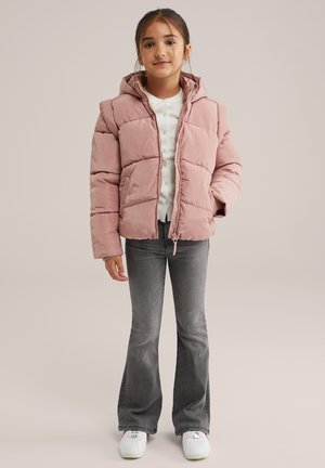 Giacca a vento di un delicato rosa soft con cappuccio, caratterizzata da sezioni trapuntate. Abbinata a jeans grigi svasati e sneakers bianche. Semplice camicia con bottoni sotto.