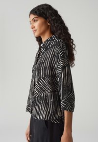 Blusa a righe verticali in bianco e nero con maniche lunghe, colletto e dettagli con bottoni. Realizzata in un tessuto leggero con vestibilità morbida.