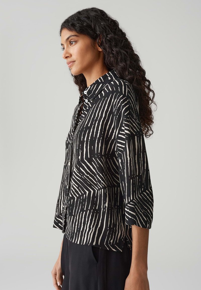 Bluzka w czarno-białe wzory, z pionowymi paskami, długimi rękawami, kołnierzykiem i guzikami. Wykonana z lekkiego materiału o luźnym kroju.
