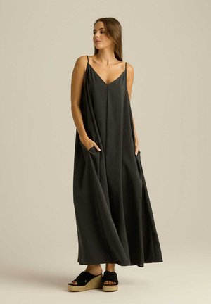 Czarna, bezrękawnikowa sukienka maxi z dekoltem w szpic, bocznymi kieszeniami i zwiewnym krojem. Nosi z czarnymi espadrylami.