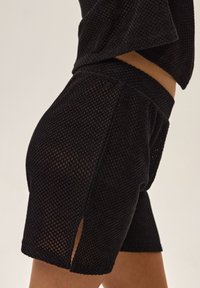 Czarne siatkowe szorty z teksturowanym wzorem, wyposażone w boczne rozporki oraz elastyczny pas dla wygody. Materiał jest przewiewny i lekki.