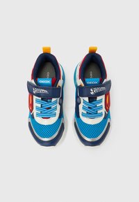 Pari lasten sinisiä, punaisia ja valkoisia tennareita, joissa on verkkomaiset päälliset, tarrakiinnitteiset remmit, joissa lukee "Superman", ja siniset nauhat valkoisella taustalla.