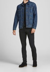 Chaqueta vaquera en azul oscuro con dos bolsillos en el pecho, cierre delantero con botones y costuras sutiles. Combinada con jeans ajustados negros y zapatos negros.