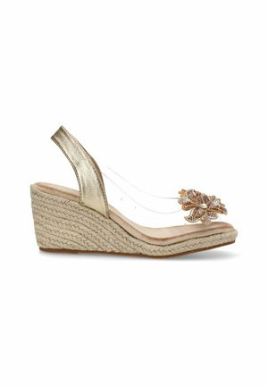 Sandalia cuña metálica dorada con base de esparto, correas transparentes y un adorno floral joyado en la puntera.
