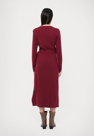 Long maroon dress made of soft fabric, with a fitted silhouette and a tie belt at the waist. Features long sleeves and a hem that falls below the knee.
